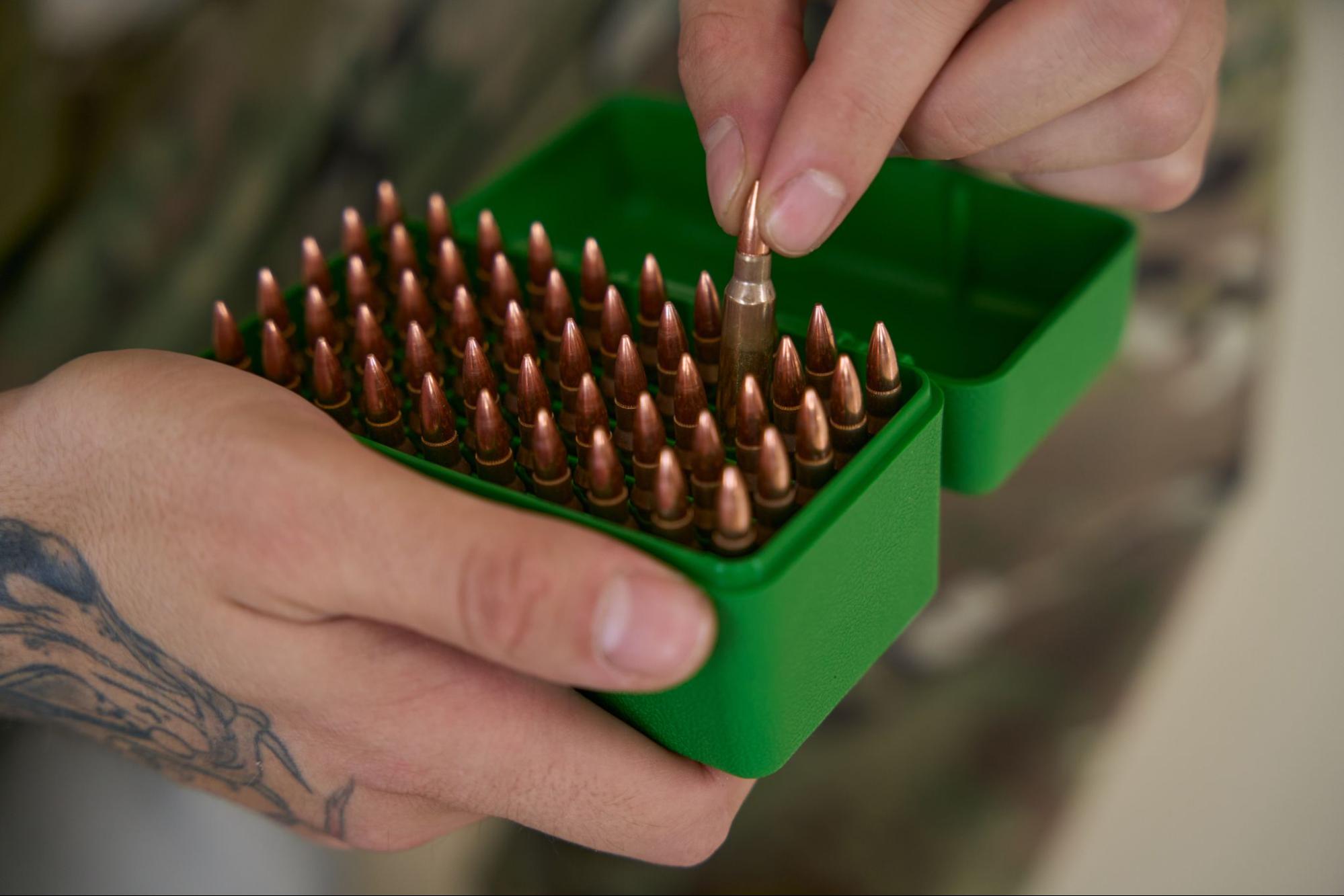 Hand placing bullets in green ammo box.