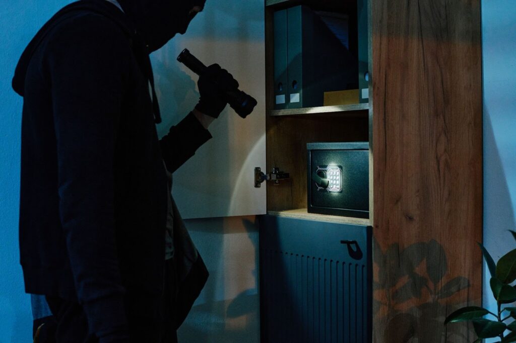 Burglar with flashlight searching cabinet safe